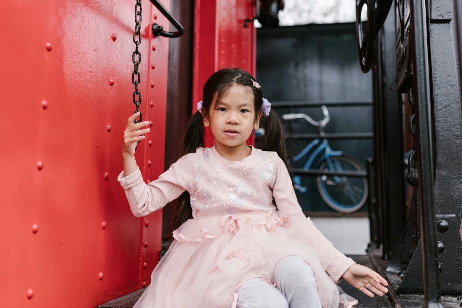 A young girl in a pink dress sits on a vintage train, evoking a sense of adventure and nostalgia.